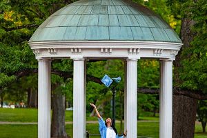 graduate tosses cap while standing in from of the UNC Well